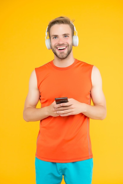 Heureux jeune homme en tenue de sport portant des écouteurs modernes écoutant de la musique pendant l'entraînement, utilisez l'application d'achat de fitness pour smartphone