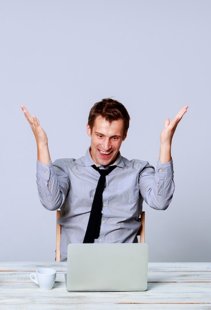 Heureux jeune homme travaillant sur ordinateur portable au bureau sur fond gris