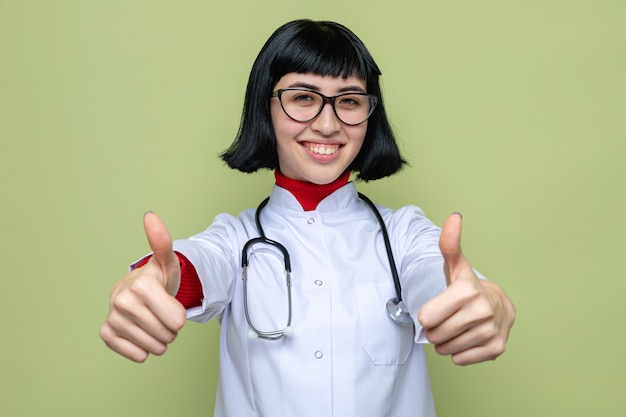 Heureux jeune jolie femme de race blanche en uniforme de médecin avec stéthoscope pouce vers le haut avec deux mains