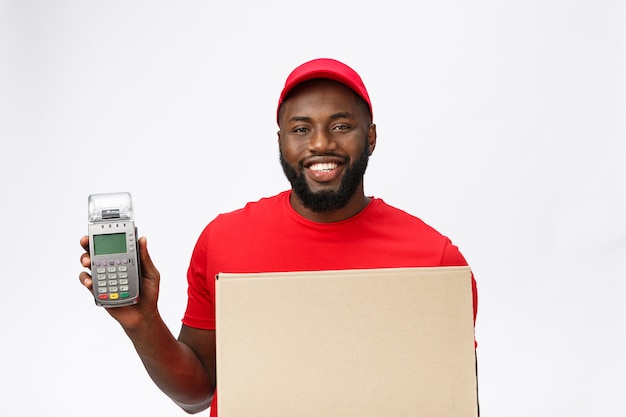 Heureux jeune livreur afro-américain tenant une machine de paiement par carte électronique et un produit de livraison.