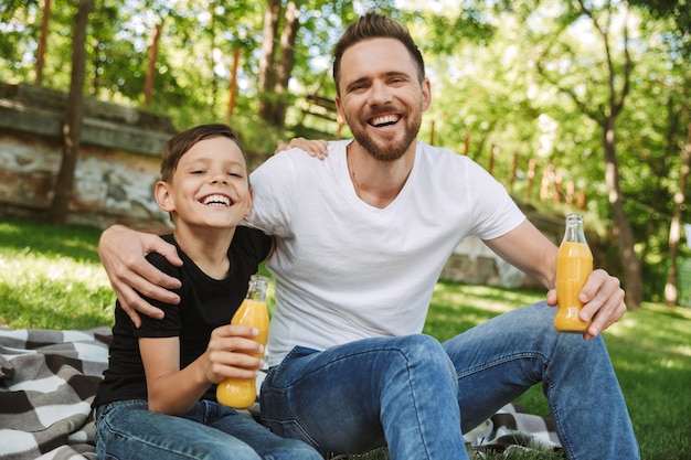 Heureux jeune père assis avec son petit fils à l'extérieur, boire du jus.