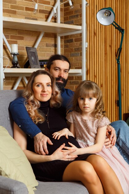 Heureux Jeune Père, Mère Et Fille Assis Sur Un Canapé En Osier à La Maison. L'image D'une Famille Heureuse Attend Le Deuxième Enfant, Studio