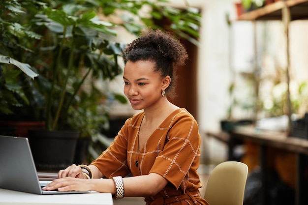 Heureux jeune propriétaire d'une orangerie ou d'une serre moderne assis devant un ordinateur portable