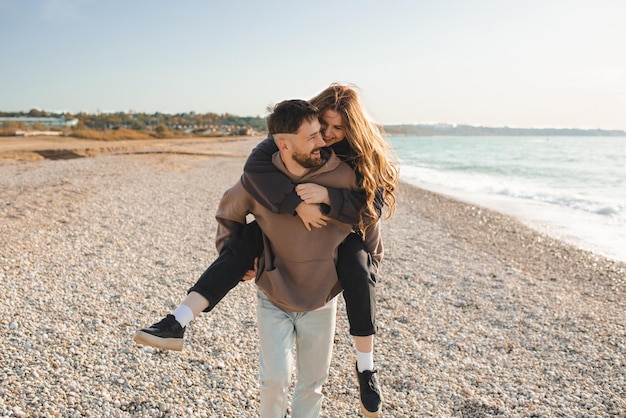 Heureux jeunes adultes couple s'amusant à la plage sur fond de mer ensemble Homme souriant porter jolie femme sur l'océan