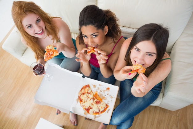 Heureux jeunes amies avec pizza et vin sur canapé