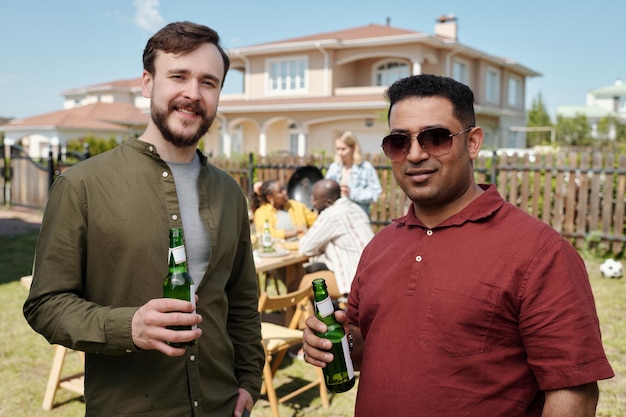 Heureux jeunes amis masculins interraciaux avec des bouteilles de bière en regardant la caméra