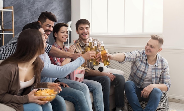 Heureux jeunes amis tinter des bouteilles de bière assis sur un canapé