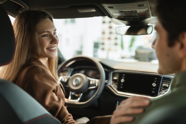 Heureux jeunes conjoints caucasiens achetant une nouvelle voiture faisant un essai routier assis à l'intérieur d'une voiture moderne à