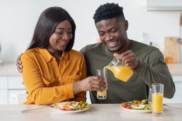 Heureux jeunes époux noirs prenant leur petit déjeuner ensemble mari versant du jus de cruche