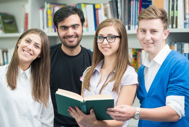 Heureux jeunes étudiants qui étudient à la bibliothèque du collège faire une recherche de travail d&#39;équipe