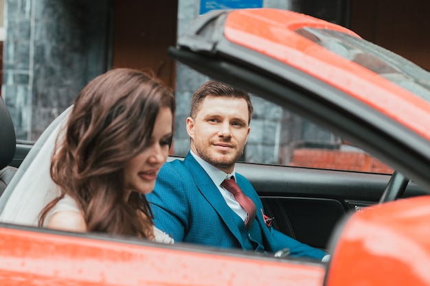 Un heureux jeunes mariés vont à la célébration dans une voiture rouge avec un toit ouvert. Concept de mariage