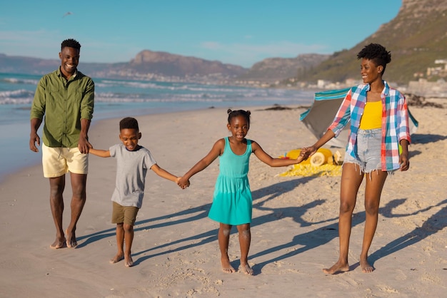 Heureux jeunes parents et enfants afro-américains se tenant la main tout en se tenant à la plage contre le ciel