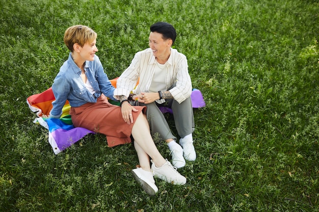 Heureux lesbiennes assis sur l'herbe verte sur le drapeau coloré et se parler pendant la journée d'été