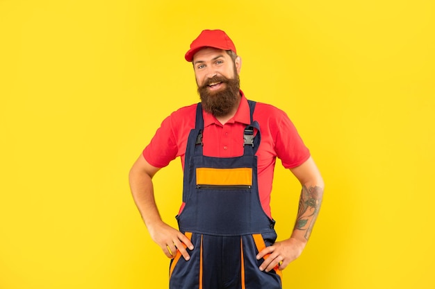 heureux livreur barbu en vêtements de travail sur fond jaune.