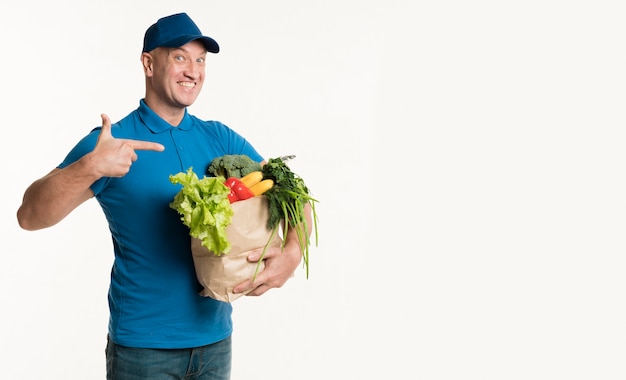 Heureux livreur pointant au sac d'épicerie à la main