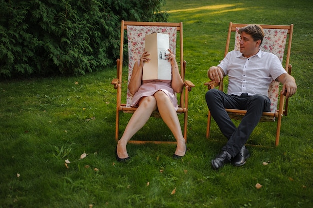 Heureux mari et femme assis sur la chaise longue dans le parc verdoyant sur le gazon