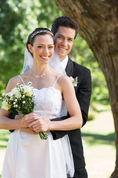 Heureux marié embrassant la mariée par derrière dans le jardin