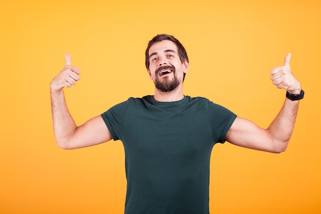 Heureux mec branché souriant montrant les pouces vers le haut sur fond jaune. L'homme à la recherche cool donne son approbation