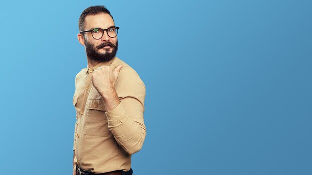 Heureux mec hipster barbu pointe de côté sur un espace vide isolé sur bleu