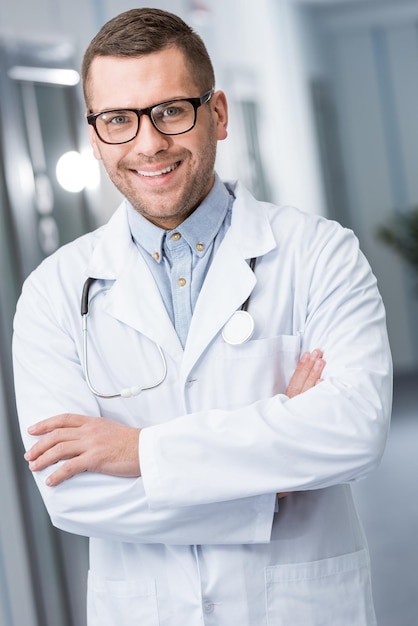 Heureux médecin à lunettes debout avec les bras croisés