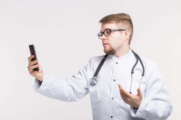 Heureux médecin de sexe masculin faisant selfie photo avec smartphone sur fond blanc