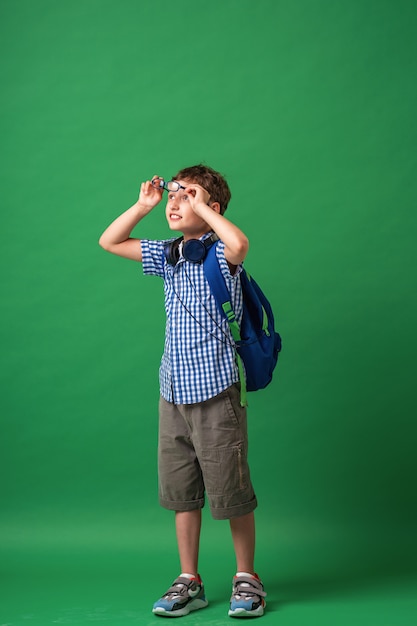 Heureux mignon garçon intelligent dans des verres avec sac d'école et casque