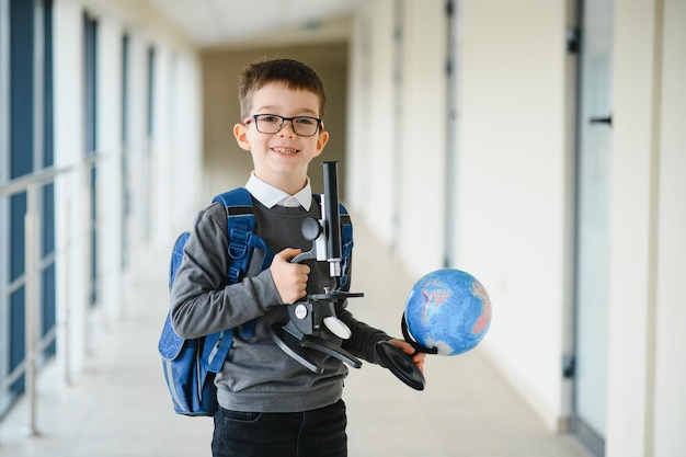 Heureux mignon garçon intelligent dans des verres avec sac d'école et livre à la main Première fois à l'école Retour à l'école