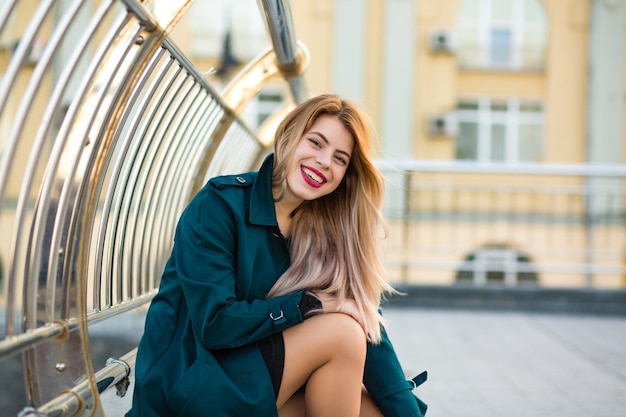 Heureux modèle blonde portant un manteau vert posant dans la rue. Espace pour le texte