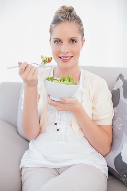 Heureux modèle frais tenant une salade saine assis sur le canapé