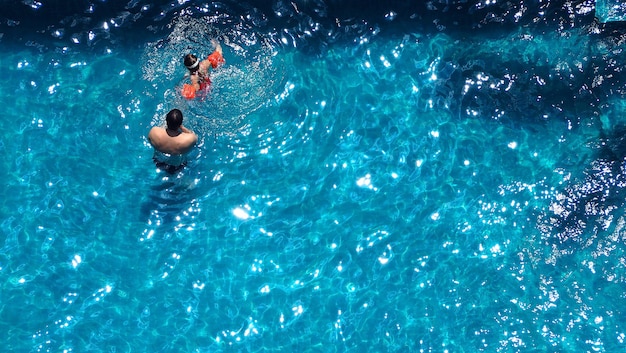 Heureux papa et jeune fille jouant ensemble dans une piscine avec bouée de sauvetage pour la sécurité par une journée d'été ensoleillée.