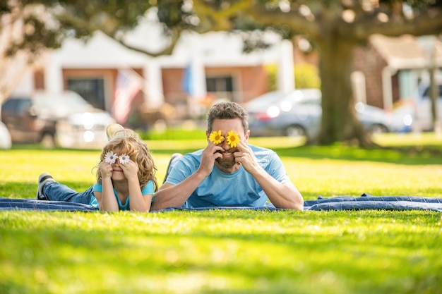 Heureux papa avec son fils jouer avec des fleurs ensemble sur le lien familial de l'herbe du parc verdoyant