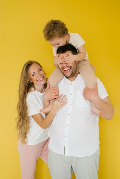 Heureux parents étreignant leur fils exprimant des sentiments chaleureux d'amour L'enfant est assis sur le cou du père S'amuser famille fond jaune isolé