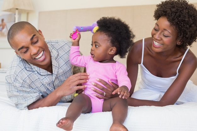 Heureux parents jouant avec bébé fille sur le lit ensemble