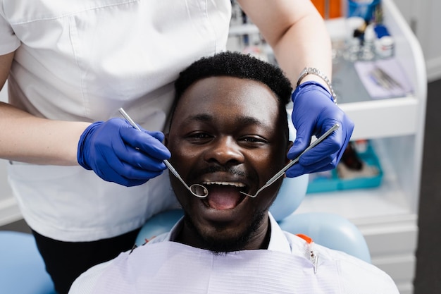 Heureux patient afro-américain de dentisterie Traitement des dents Bel homme africain assis dans un cabinet dentaire et souriant Dentiste en visite et consultation