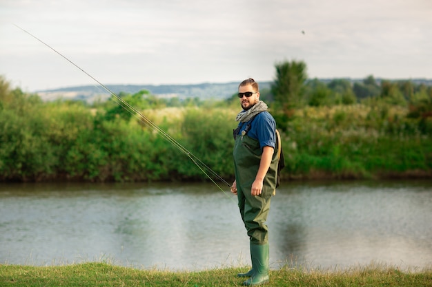 Heureux pêcheur avec costume spécial et canne à pêche près de la rivière