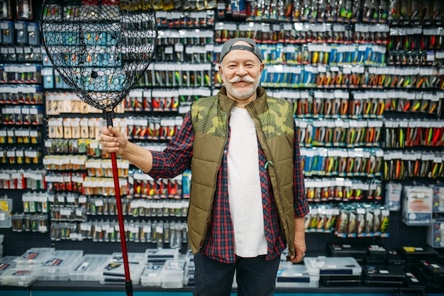 Heureux pêcheur tient un filet dans un magasin de pêche, des hameçons et des boules