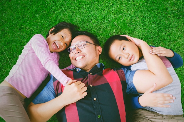 Heureux père couché avec ses enfants sur l'herbe verte