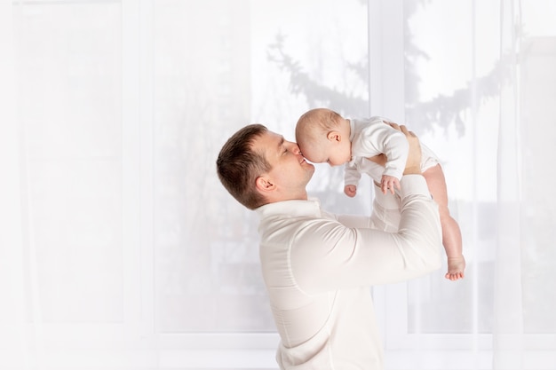 Heureux père embrasse bébé nouveau-né à la maison par la fenêtre, heureux concept de famille aimante, fête des pères