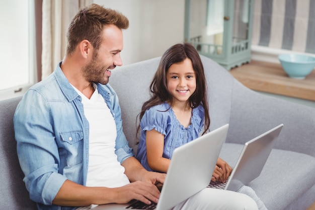 Heureux père et fille à l'aide d'un ordinateur portable sur un canapé