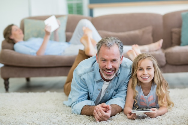 Heureux père et fille à l'aide de téléphone portable en position couchée sur le sol dans le salon