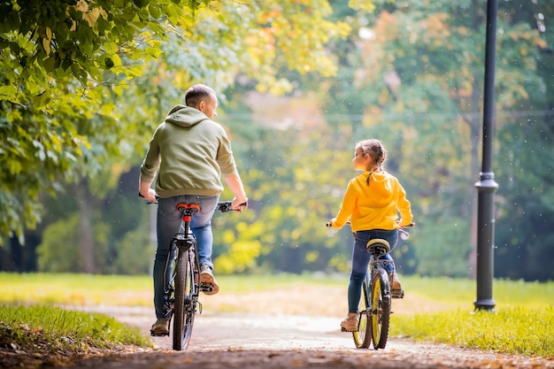 Heureux père et fille faire du vélo dans le parc d'automne aux beaux jours