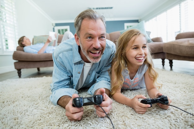 Heureux père et fille jouant au jeu vidéo en position couchée sur le sol dans le salon