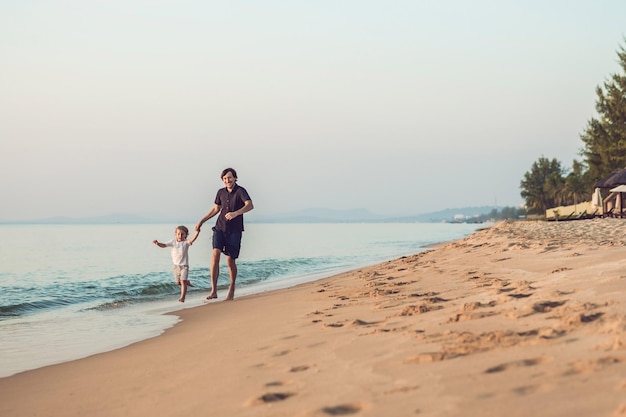 Heureux père et fils ayant du temps en famille de qualité sur la plage au coucher du soleil pendant les vacances d'été. Mode de vie, vacances, bonheur, concept de joie.