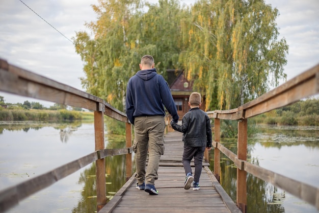 Heureux père et fils étreignant et jouant ensemble dans la nature verte Maison de pêcheur avec un pont piétonnier en bois sur une petite île au milieu du lac