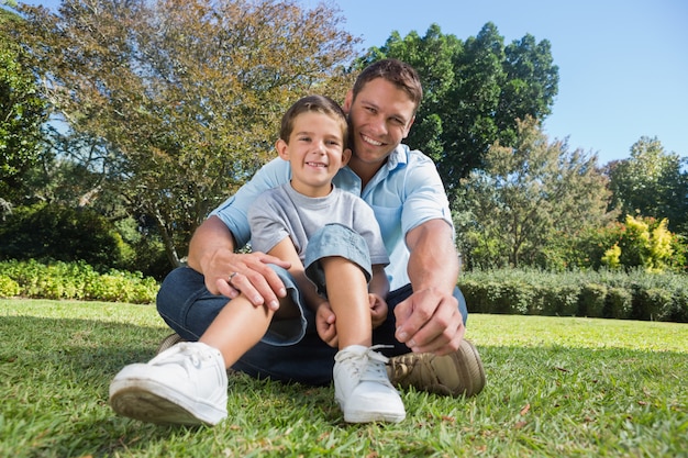 Heureux père et fils souriant à la caméra dans un joli parc sous le soleil