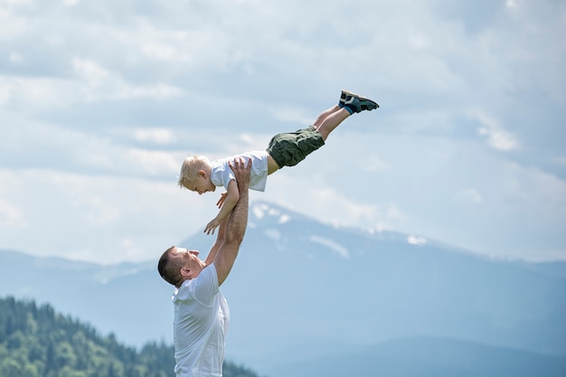 Heureux père jette un petit fils dans la forêt verte, les montagnes et le ciel avec des nuages. Amitié de paternité