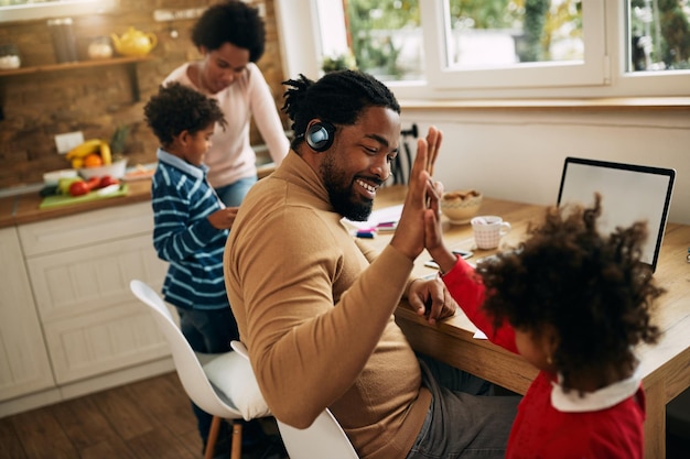 Photo heureux père noir donnant highfive à sa fille tout en travaillant à la maison