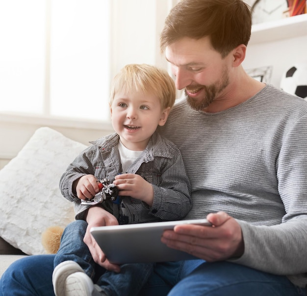 Heureux père et petit fils jouant sur tablette numérique assis sur un canapé à la maison