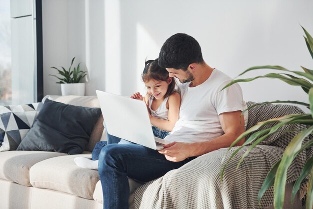 Heureux père avec sa fille passant du temps libre avec un ordinateur portable à la maison ensemble