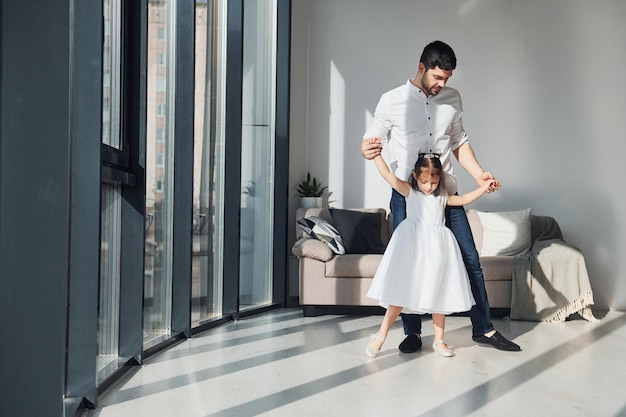 Heureux père avec sa fille en robe apprenant à danser ensemble à la maison